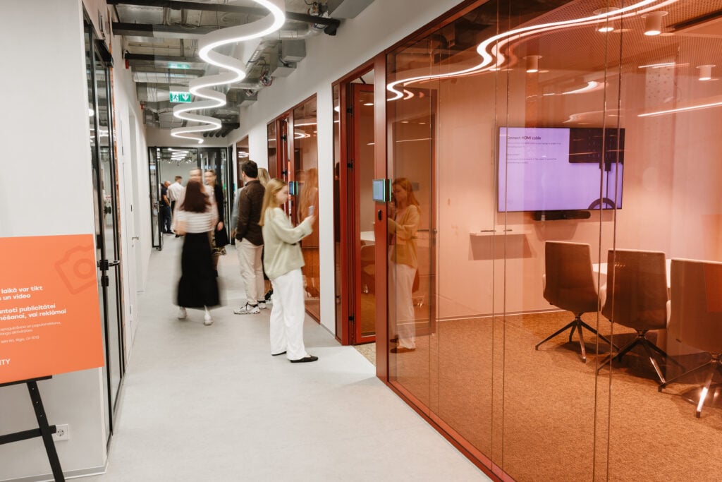 Modern office hallway with people and glass meeting rooms.